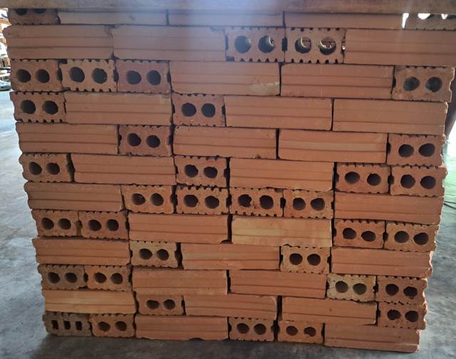 A stack of orange clay bricks. Some show their long grooved side, some show the end with two round holes.
